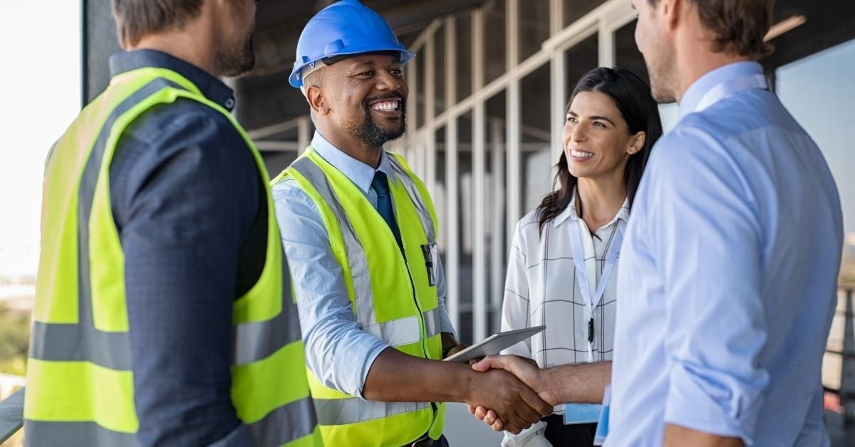 man in construction hat, holding tablet, shaking hands with another man
