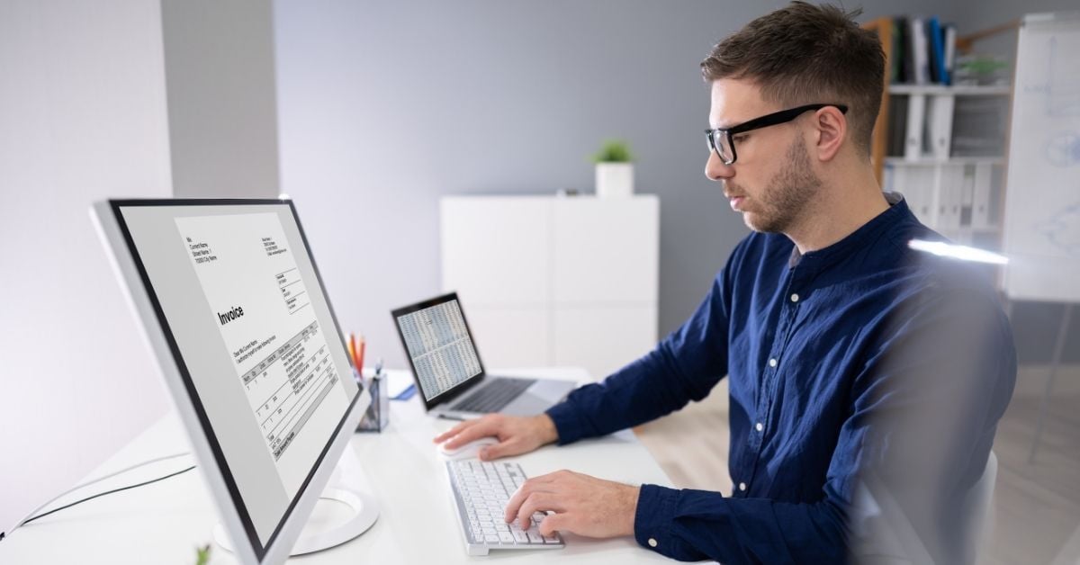 young man at computer typing and viewing an invoice