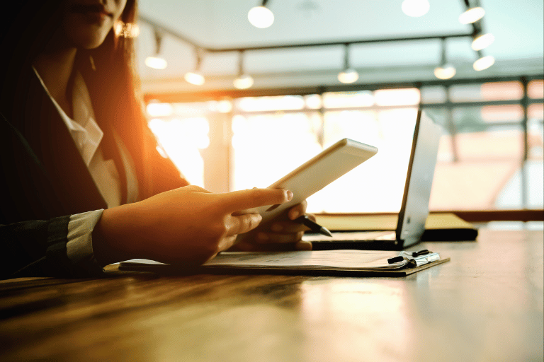 woman at desk looking at tablet and laptop