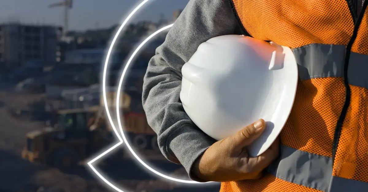 man on construction site in orange safety vest holding hard hat with ncs logobehind it