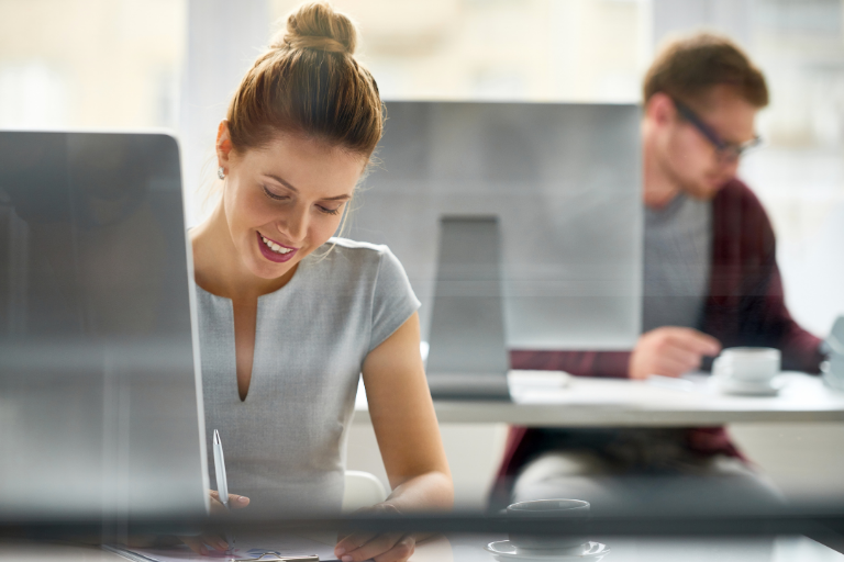 Commercial Debt Recovery professional woman at computer desk writing with pen, man in background at computer