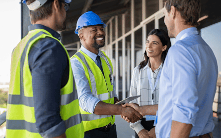man in construction hat, holding tablet, shaking hands with another man